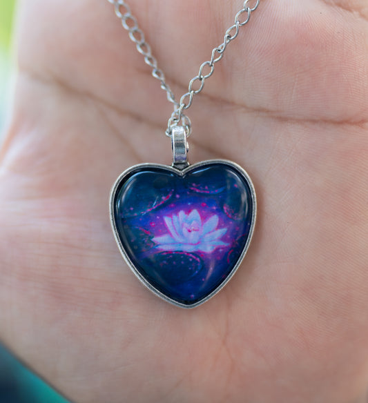 Heart-shaped pendant with a pink flower design on a silver chain held in a hand.