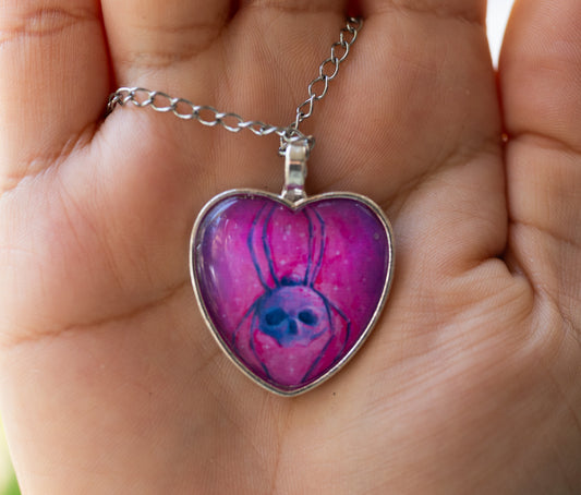 Heart-shaped pendant with a spider design held in a hand
