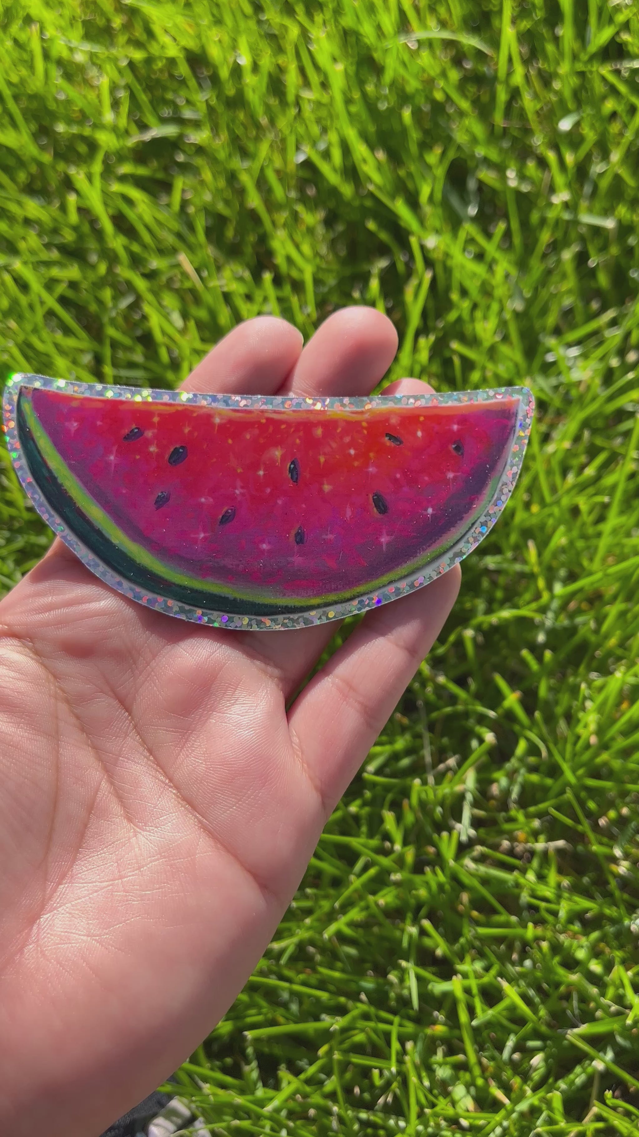 Video of a bright neon pink, red, and purple watermelon painting with seeds. Outlined with glitter. The sticker is moved back and forth to show the glitter effect. 